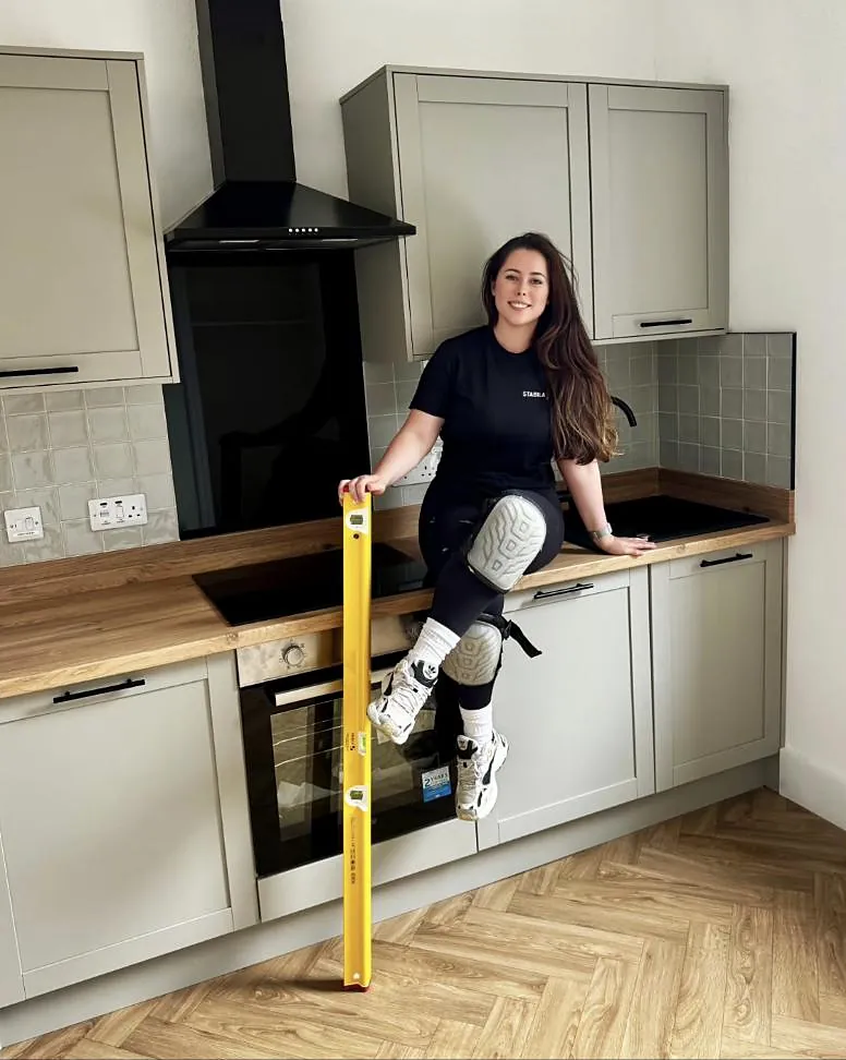 Emma Watson sitting on a kitchen worktop holding a yellow spirit level