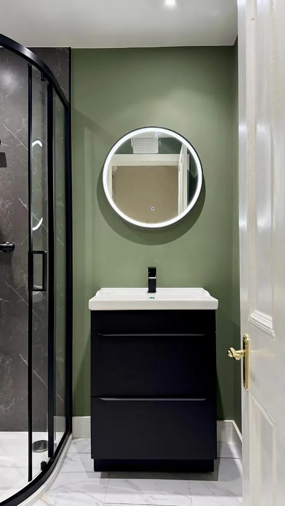 Sage green bathroom with a round LED mirror and black vanity