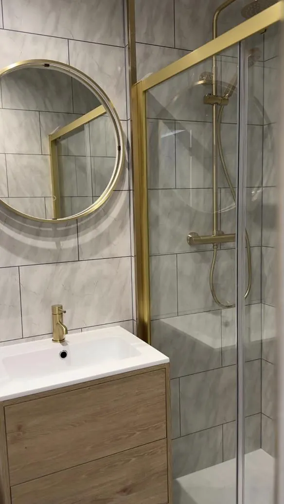Bathroom with brushed brass shower, round brass mirror and oak vanity