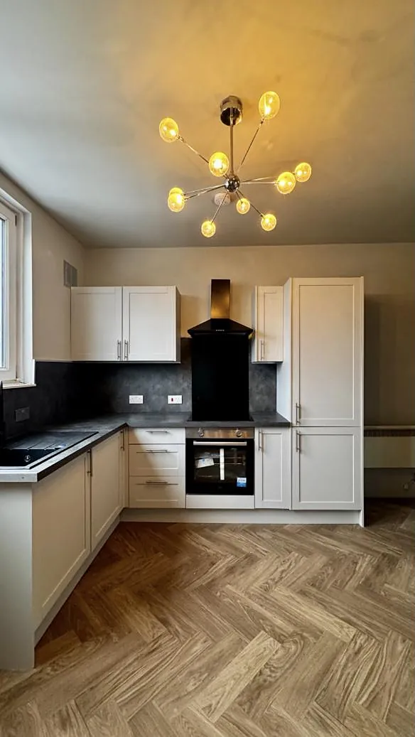 Cream shaker kitchen with a dark worktop, glass chandelier and herringbone floor