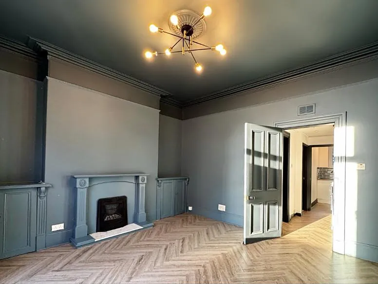 A refurbished living room at Howburn Place with a dark ceiling, brass sputnik light, painted fireplace and herringbone floor