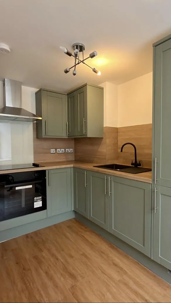 Sage green shaker kitchen with oak worktops and a black tap